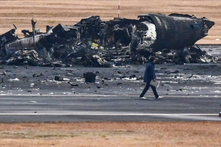 Homem caminha próximo de destroços de avião que colidiu na pista de aeroporto em Tóquio