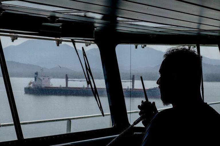 Sombra de homem falando em rádio, observando janela de navio
