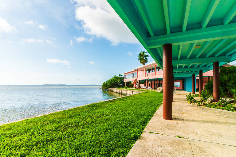 Sob a passarela de um prédio rosa e azul de dois andares com vista para a Baía da Flórida sob um céu azul brilhante.