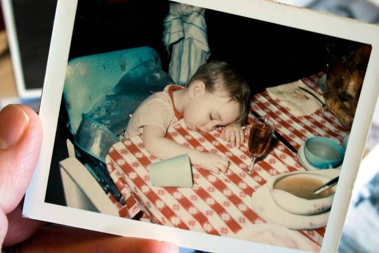 Mão segura foto polaroid de criança dormindo após refeição em cima da mesa