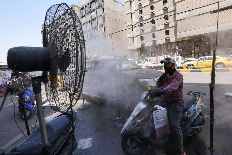 Motociclista se refresca em frente à ventilador que espirra água em Bagdá, Iraque