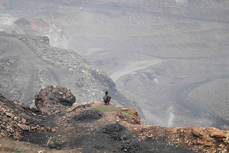 Homem de costas, sujo de fuligem, sentado à beira de um grande buraco de uma mina de carvão