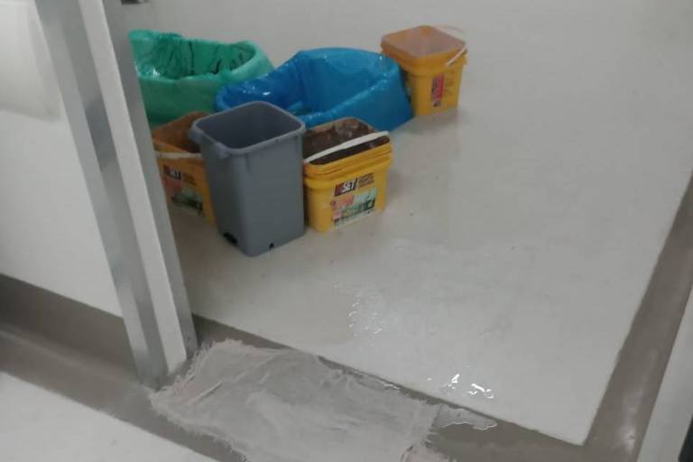 Imagem de ala de hospital. O chão está molhado e há panos e baldes para contenção da água da chuva.