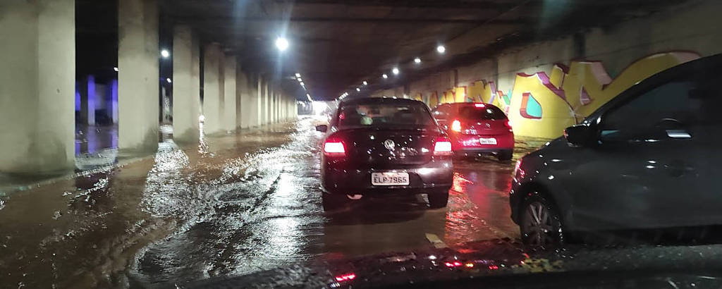 carros transitam por túnel à noite com rua alagada 