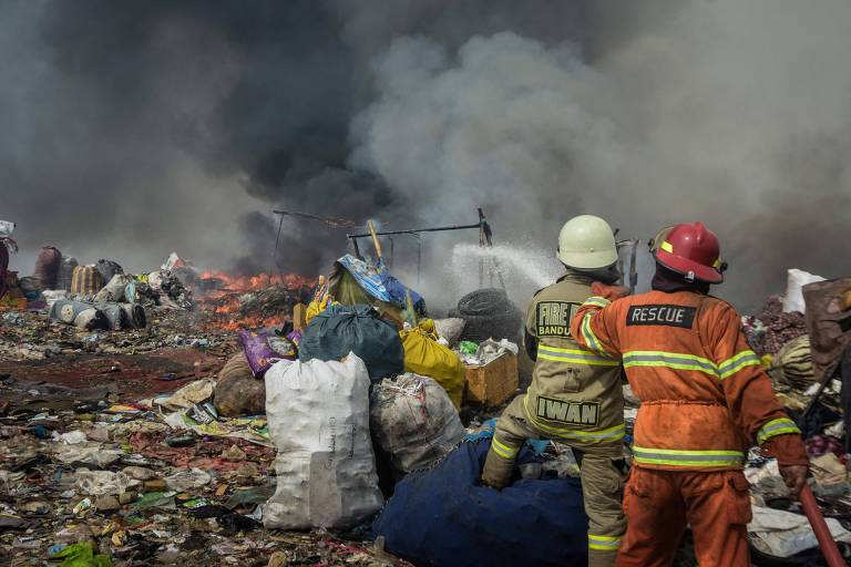 Bombeiros trabalham para extinguir fogo em lixão, de onde sobe fumaça escura