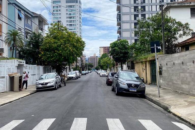 Foto mostra rua com carros estacionados, faixa de pedestres e prédios ao fundo