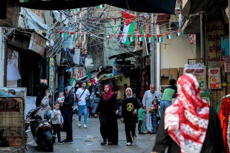 Pedestres caminhando em viela com várias pequenas bandeiras palestinas penduradas