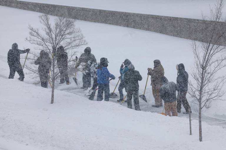 Grupo de pessoas limpa a neve de uma calçada em Des Moines, capital de Iowa; o Serviço Meteorológico local disse esperar 'um clima de inverno com risco de vida começando com forte neve' e pediu que a população local se planeje com cautela para a temporada de neve e baixas temperaturas