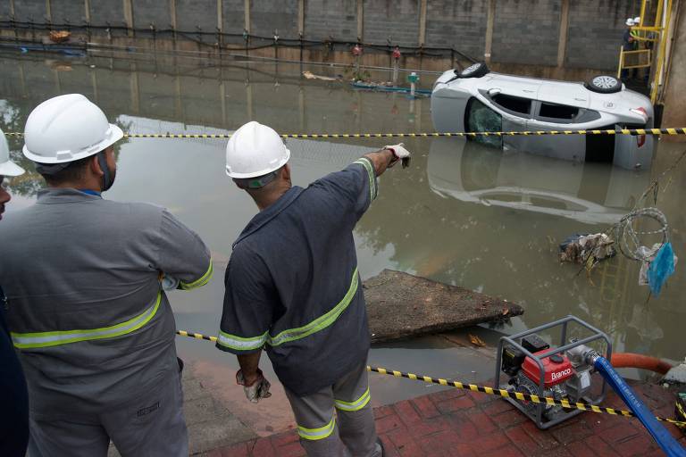 Trabalhadores observam um carro na água e a destruição causada pelas fortes chuvas no Rio de Janeiro