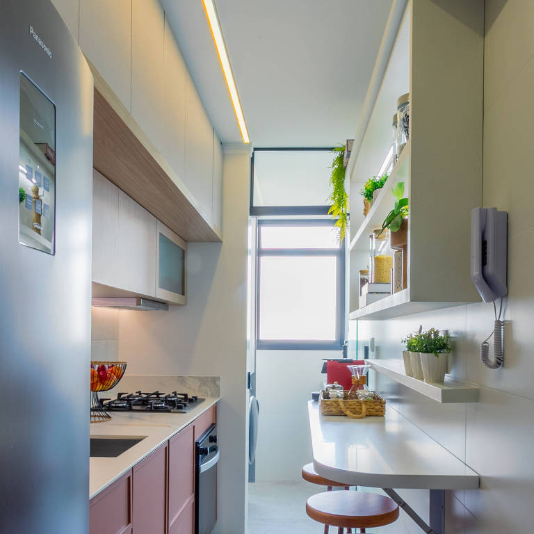 Cozinha estreita com geladeira, bancada da pia e cooktop do lado esquerdo e uma bancada com bancos da outra