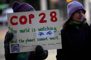 FILE PHOTO: Climate activist holds a placard during a vigil to mark the opening day of the COP28 summit outside the offices of the BBC in Salford