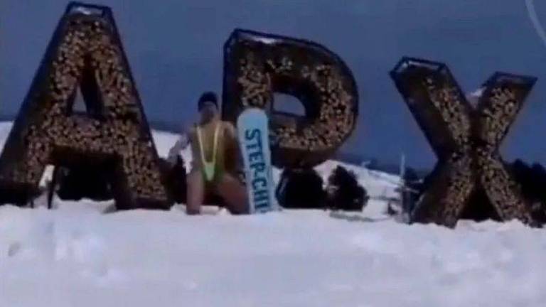 homem seminu e ajoelhado sobre a neve segura um snowboard diante de letreiro em que se lê 'APX' 