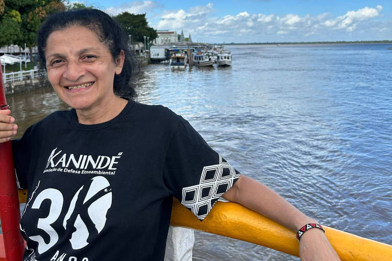 A indigenista Neidinha Suruí; ela usa uma camiseta preta com o nome da ONG Kanindé, da qual é líder, e que atua em defesa dos povos originários; na foto, Neidinha está sob uma ponte e ao fundo é possível ver um rio; ela sorri