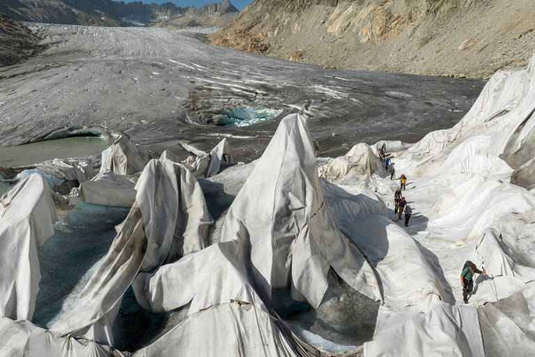 Vista aérea de grupo de pesquisadores caminhando por uma parte da geleira coberta com lonas para retardar o derretimento