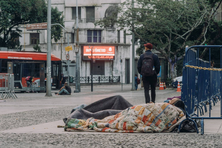 moradores de rua se cobrem com cobertores deitados em uma calçada