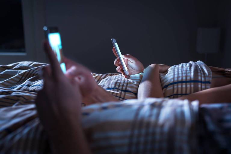 Duas pessoas deitadas na cama usando celulares