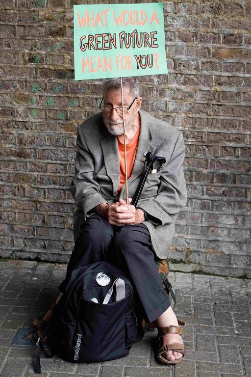 Homem grisalho, sentado e segurando uma bengala, segura placa de papel verde onde se lê "O que um futuro verde significaria para você?"