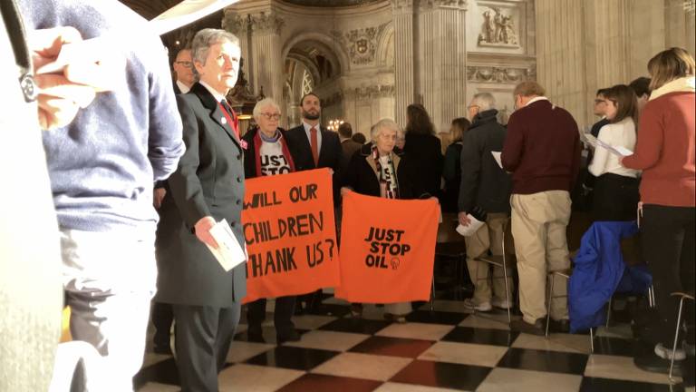 Duas mulheres idosas segurando cartazes laranjas contra combustíveis fósseis  interrompem celebração religiosa em catedral