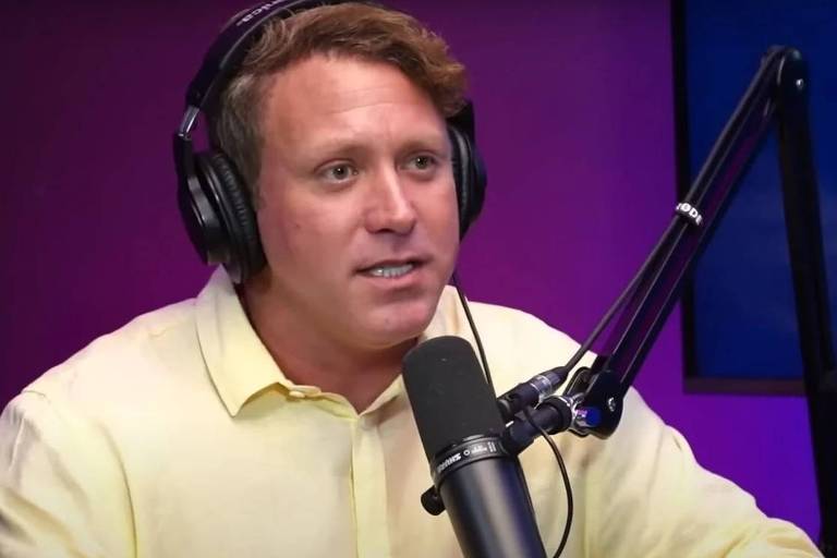 Em foto colorida, homem de camisa amarela dá entrevista para um podcast