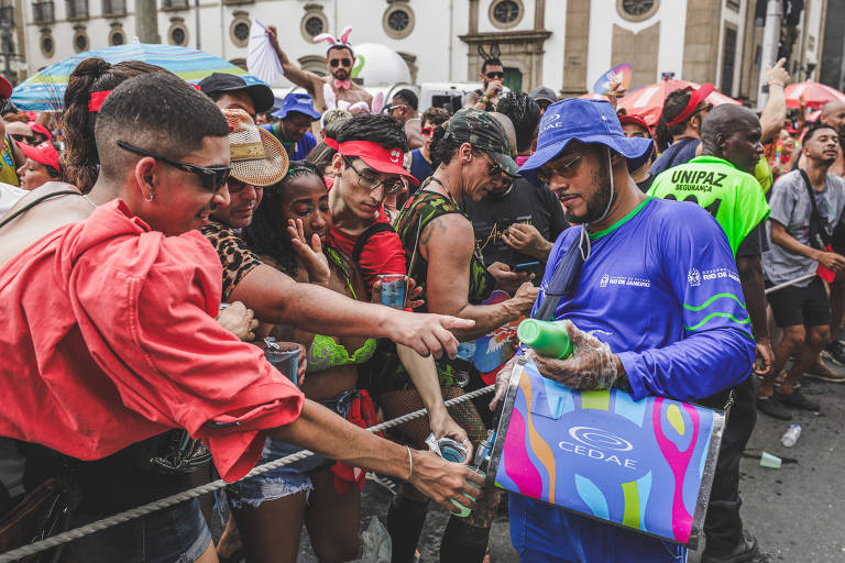 Funcionário da Cedae distribui água para foliões durante o Carnaval de blocos do Rio; no bloco Carrossel de Emoções