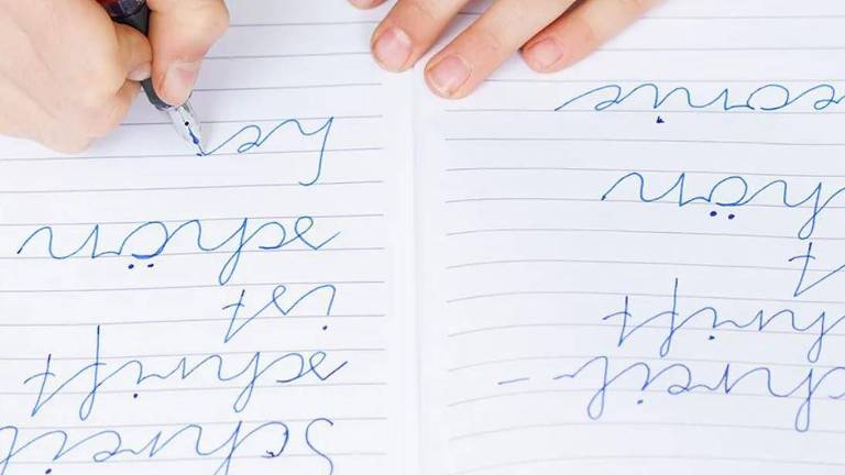 foto tirada de cima, em ângulo reto, mostra mão escrevendo sobre folha de papel com caneta 