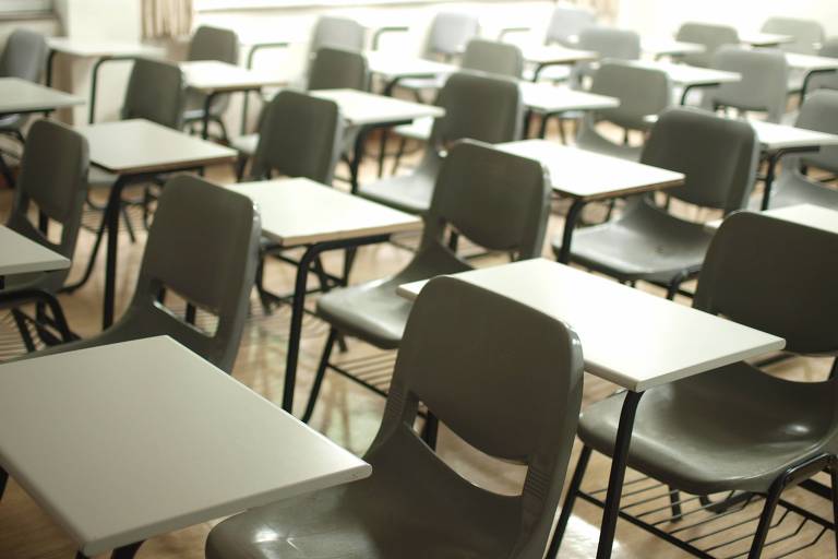 A imagem mostra uma sala de aula com mesas vazias