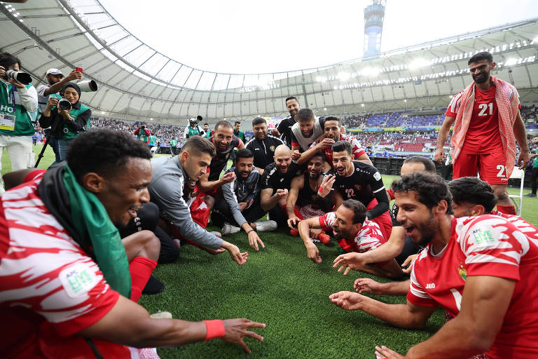Sentados no campo do estádio Khalifa, no Qatar, e mostrando felicidade, jogadores da Jordânia fazem o gesto de comer com as mãos para festejar a classificação do país para as quartas de final da Copa da Ásia