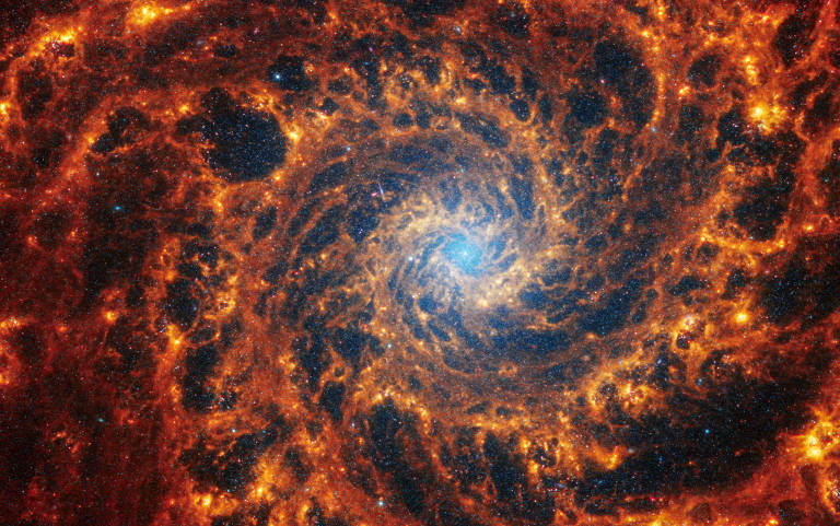 A imagem mostra uma galáxia espiral de frente densamente povoada ancorada por sua região central, que tem uma névoa azul clara