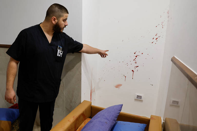 Homem aponta para manchas de sangue em parede de hospital; três palestinos foram mortos na ação israelense
