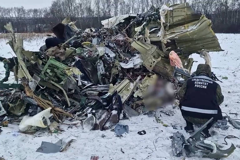 Investigador russo verifica destroços do avião derrubado na semana passada; vista de pedaço de corpo de vítima foi borrada na imagem
