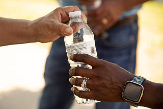 Handing off a water bottle on a hot day in Dallas, June 29, 2023. (Emil T. Lippe/The New York Times)