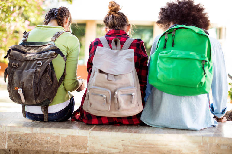 Três crianças sentadas de costas com mochilas nas costas
