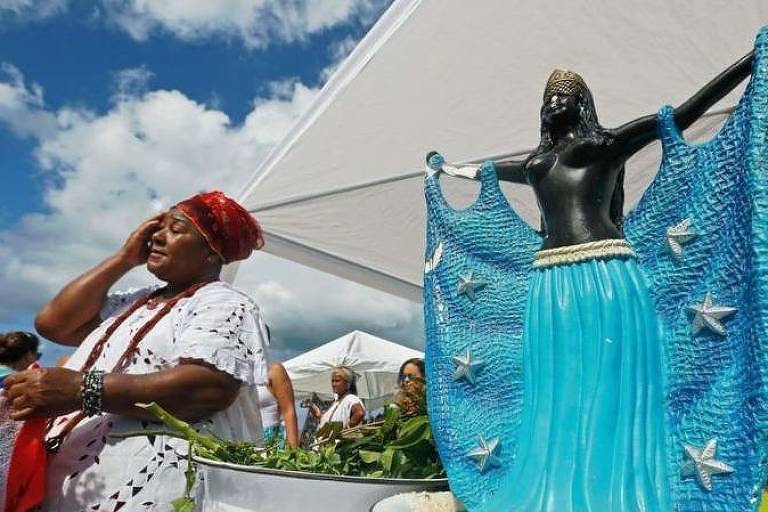 Mulher negra ao lado de estátua de Iemanjá