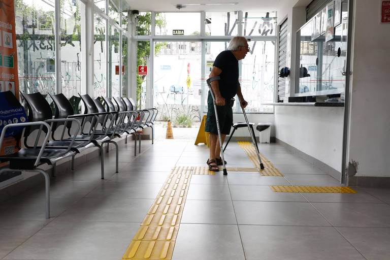 idoso caminha com muletas por sala de espera de unidade de saúde