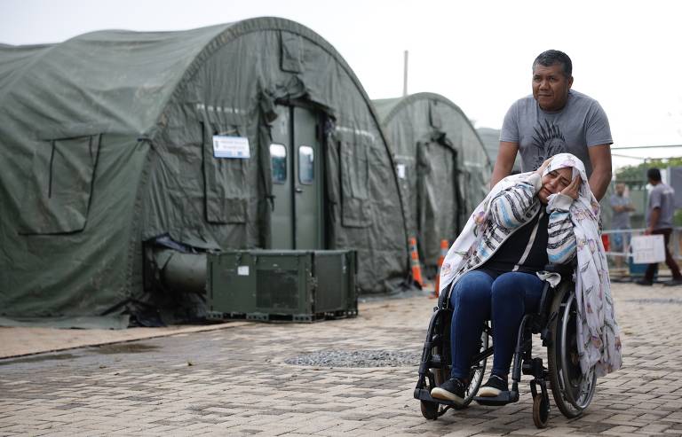 Imagem mostra homem conduzindo uma mulher em cadeira de rodas no hospital de campanha montado pelas Forças Armadas no Distrito Federal