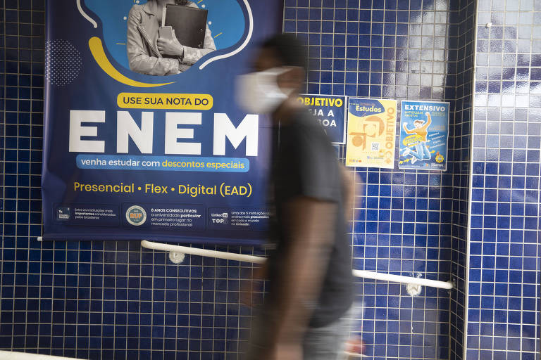 Estudante passa na frente de um cartaz chamando para a realização do Enem