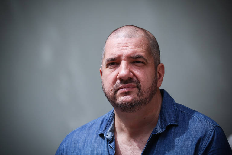 Retrato de Fabiano, um homem branco, de cabeça e barba raspadas e camisa  jeans azul; na foto, ele olha para frente