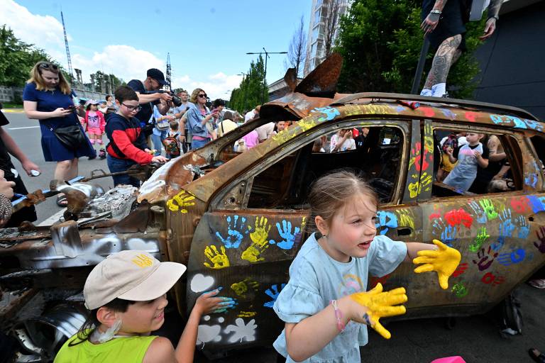 Crianças ucranianas pintam carro queimado em Butcha, que foi palco de massacre no início da guerra
