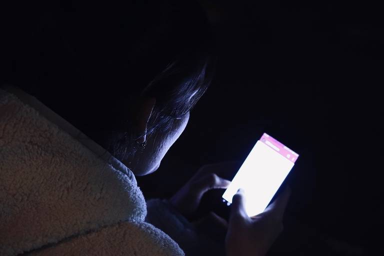 Pessoa mexe no celular em uma sala escura