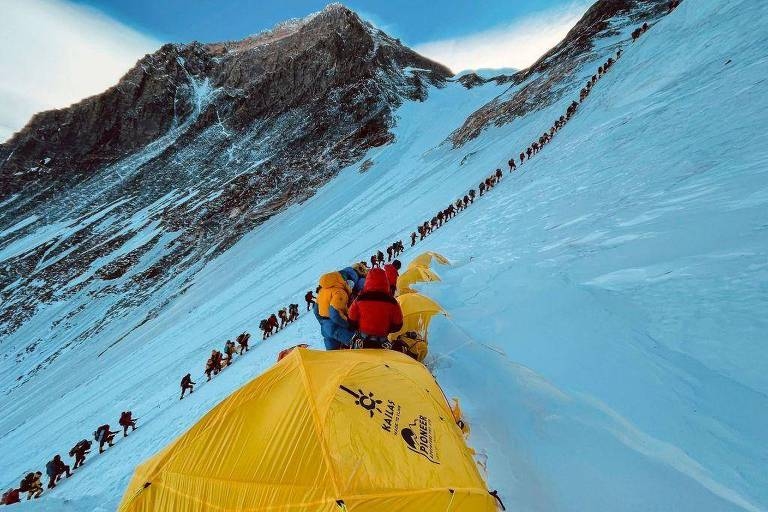 Grande fila de montanhistas alinhados enquanto escalam uma encosta durante sua subida ao cume do Monte Everest 