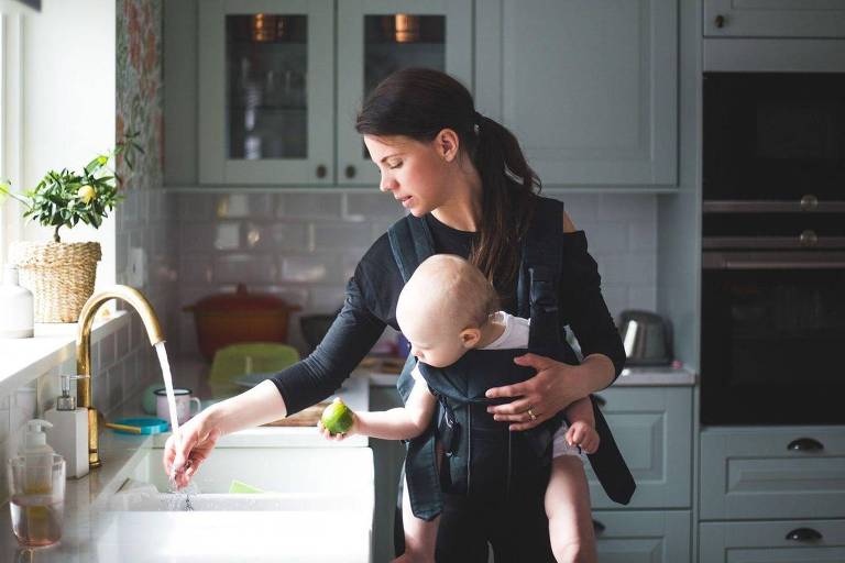 Mãe mexe em pia da cozinha enquanto carrega bebê