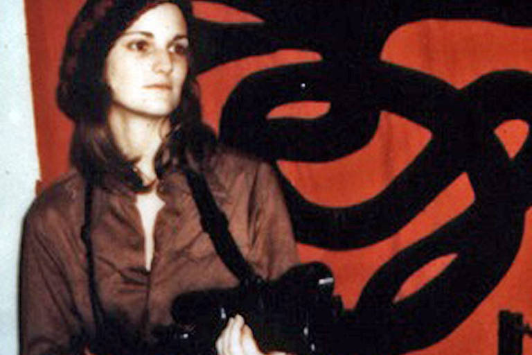 Autointitulada Tania, Patty empunha arma com a bandeira do grupo que a sequestrou ao fundo, em foto de 1974