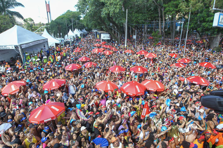 Multidão vista do alto; em meio às pessoas, há diversos guarda-sóis vermelhos com logotipo da cerveja Brahma