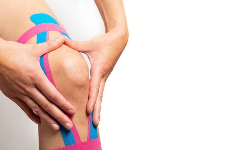 Perna de uma atleta com kinesiotape, fita muscular no joelho, nas cores rosa e azul