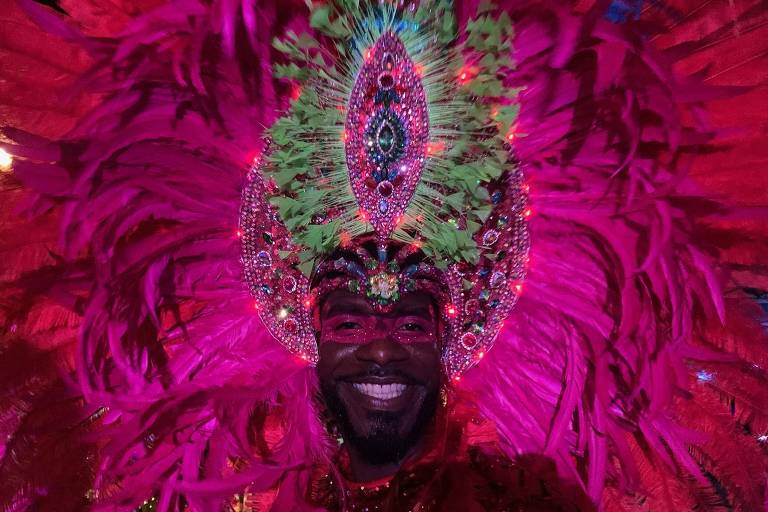 Homem negro usa máscara e fantasia rosa com penas adornando sua cabeça no Carnaval de Aruba