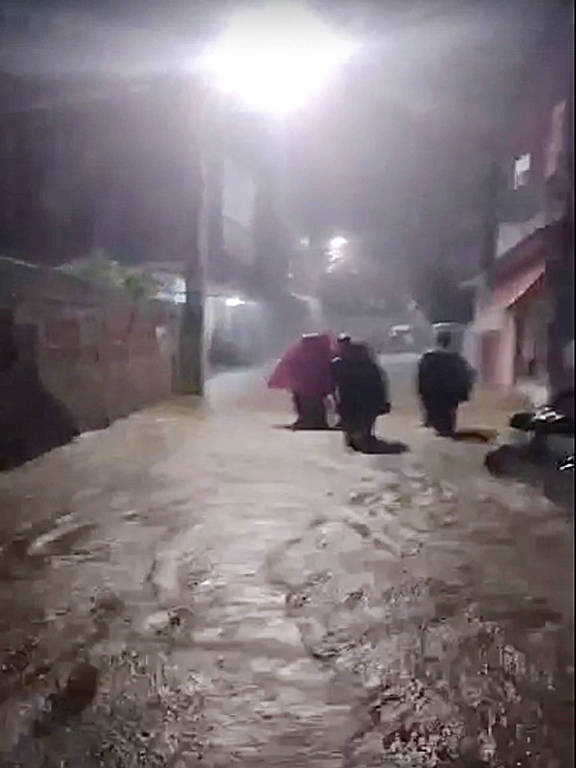 Pessoas com guarda-chuvas andam em rua alagada de Angra dos Reis em temporal de dezembro