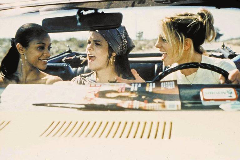 Três mulheres jovens discutem sentadas no banco da frente de um carro conversível