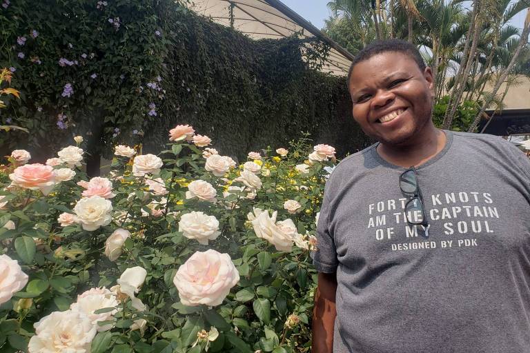 Homem negro com camiseta cinza, ao lado de um jardim florido
