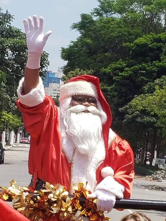 Homem negro vestido de Papai Noel com uma das mãos levantadas