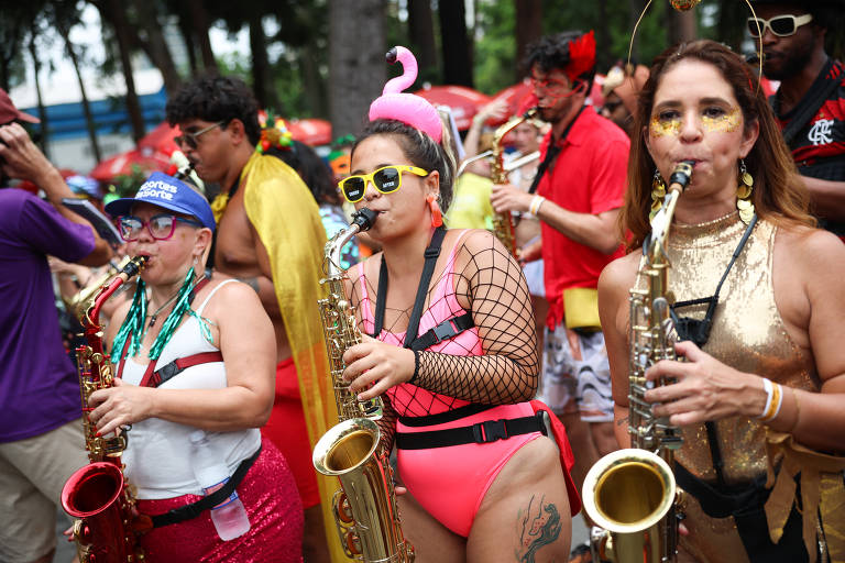Foto mostra três mulheres com fantasias carnavalescas tocando saxofones no bloco